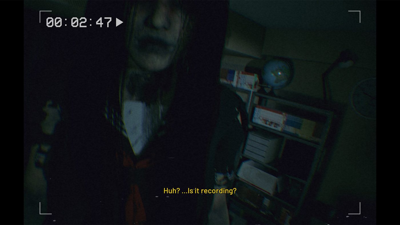 DEADCAM screenshot: a pale figure in a school uniform looms close to the camera in a dark room, with the subtitle 'Huh? ...Is it recording?'