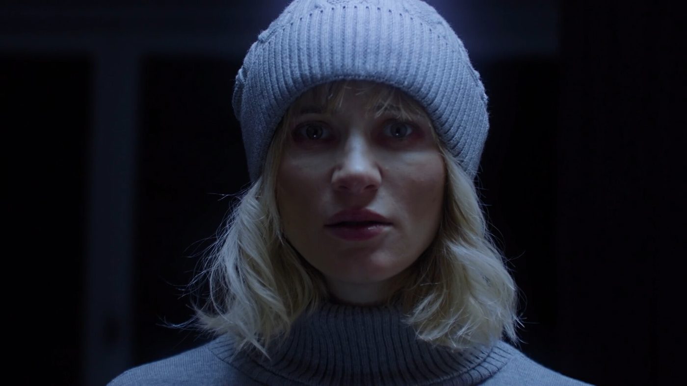 Tenebris Somnia live-action still: a pale woman in a knitted cap stares into the camera in a dark room